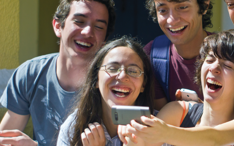 4 young people look at a phone and laugh