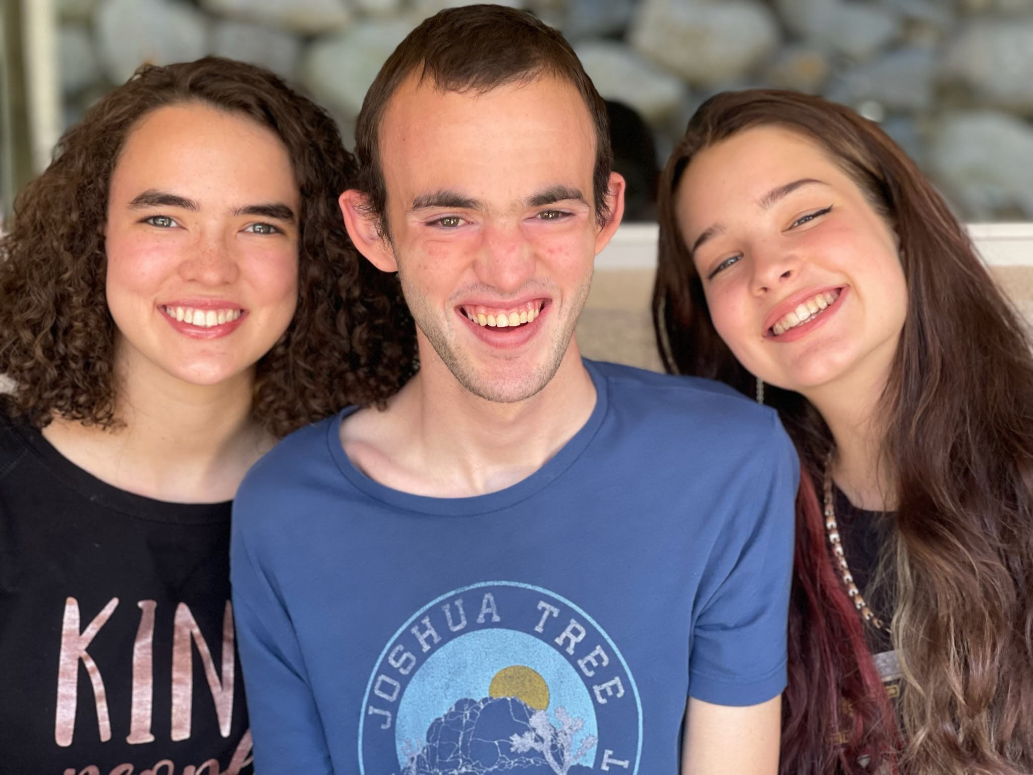 A Young man smiles with his two sisters at his side