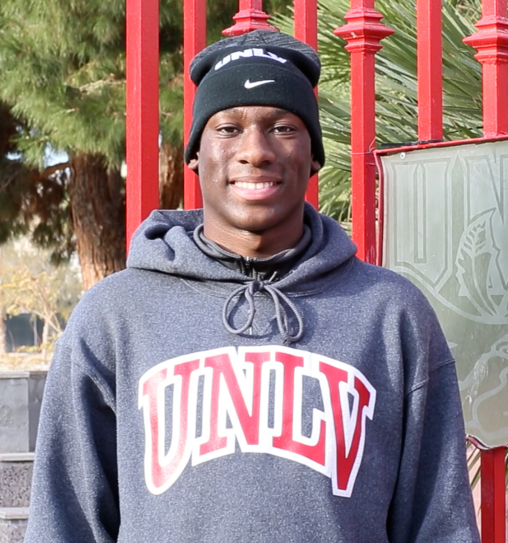A transitional student smiles in his UNLV hoodie in front of the UNLV gate