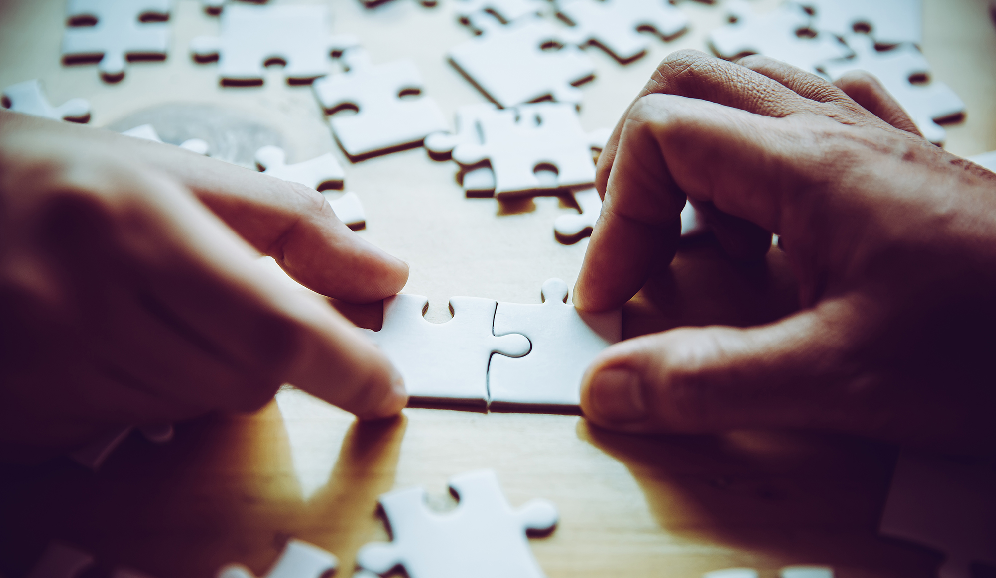 Hands playing jigsaw puzzle piece game together on wooden table