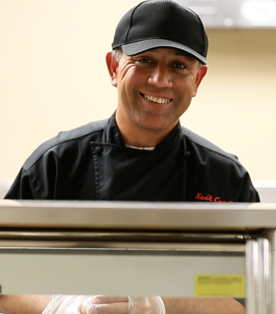 Visually impaired man wearing cafe uniform smiles warmly at the cafe service counter.