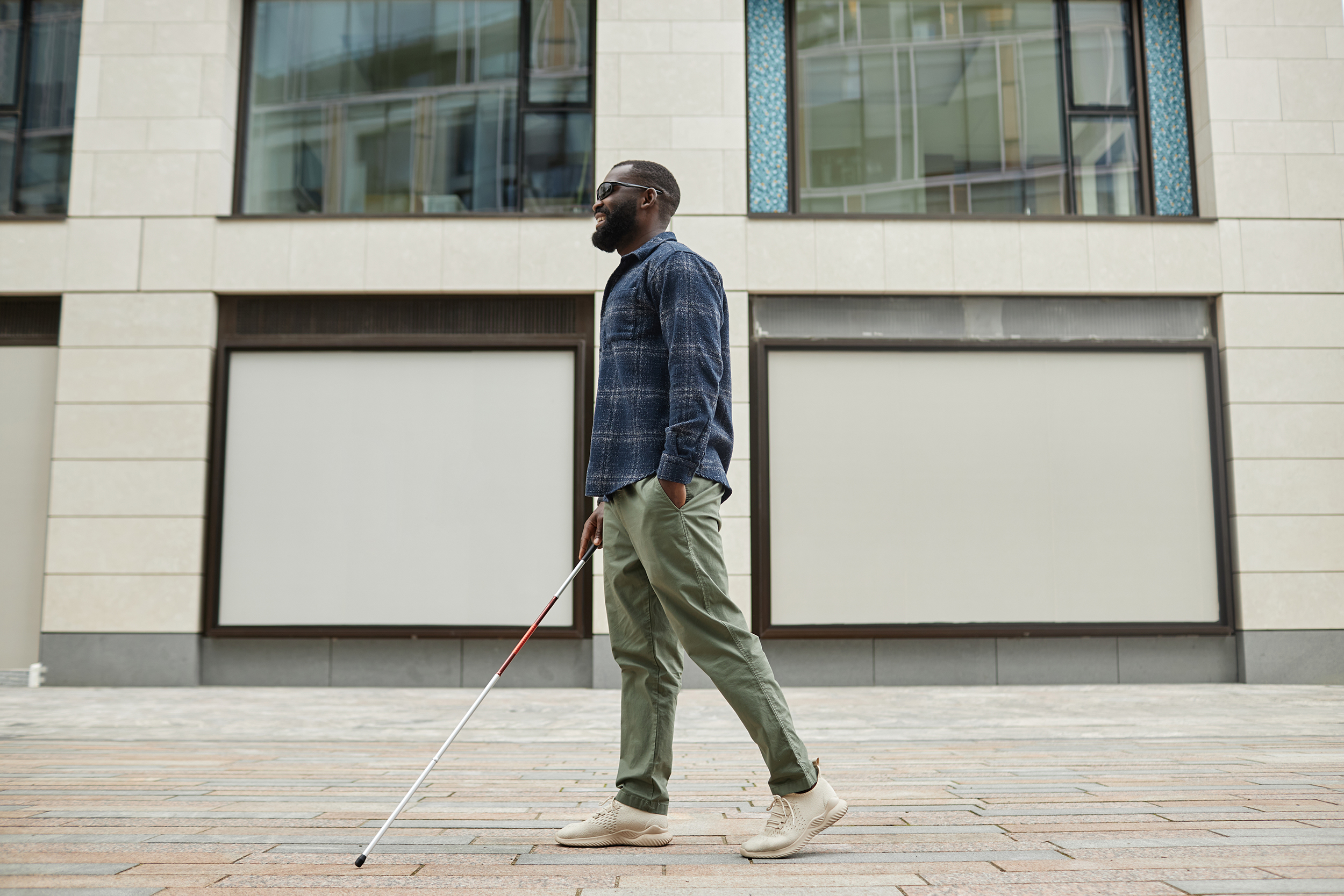 African american man smiles, walking confidently with a white cane in the city