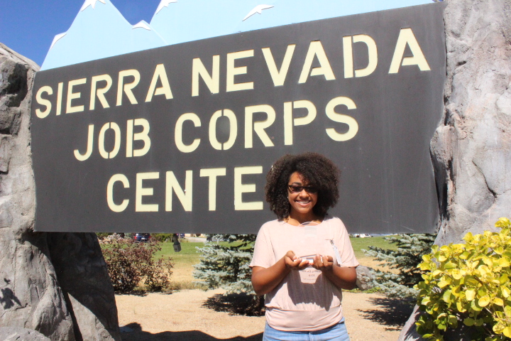 Genesis Pierre stands in fornt of the sierra nevada job corps center sign holding an award